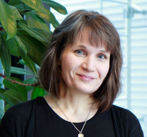 Image of smiling woman standing in front of a green plant